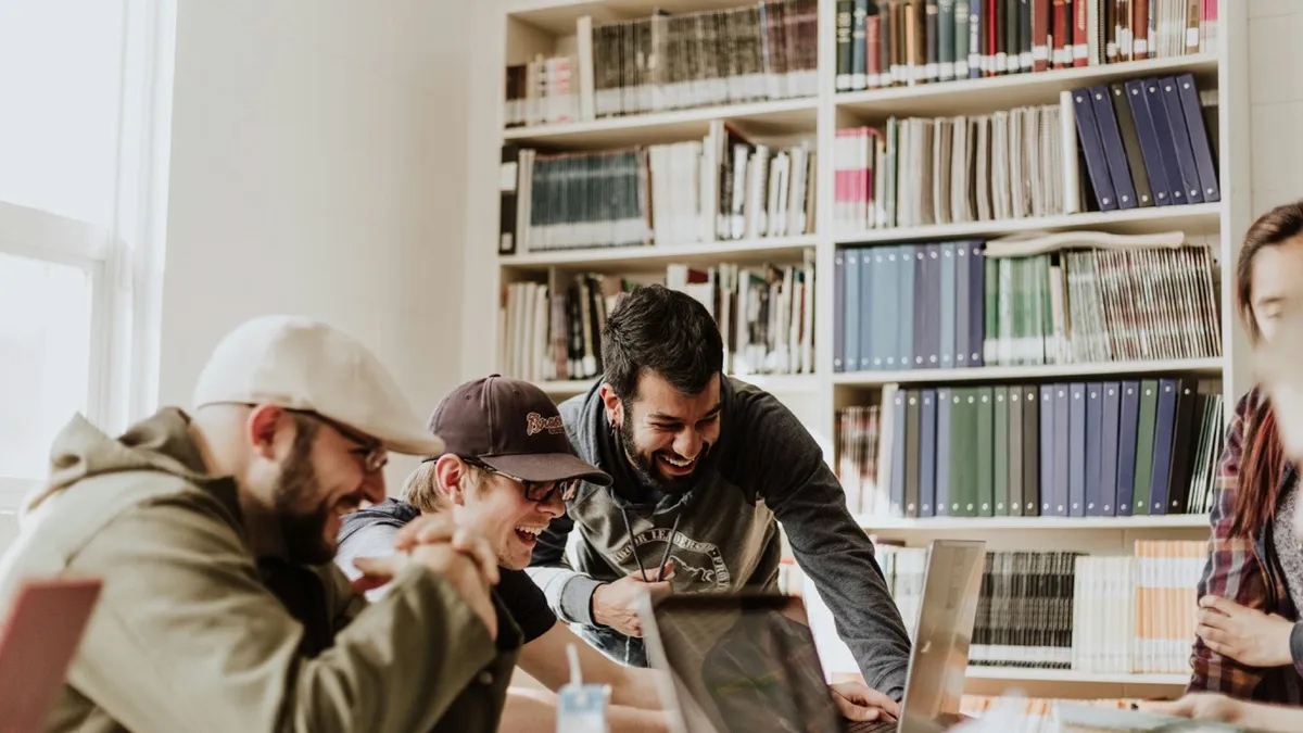 A diverse group of young professionals laughing and collaborating around laptops in a bright modern office with bookshelves illustrating brand personality